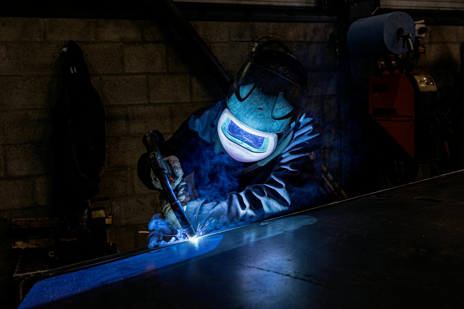 Welder in protective gear working in a workshop, sparks flying.