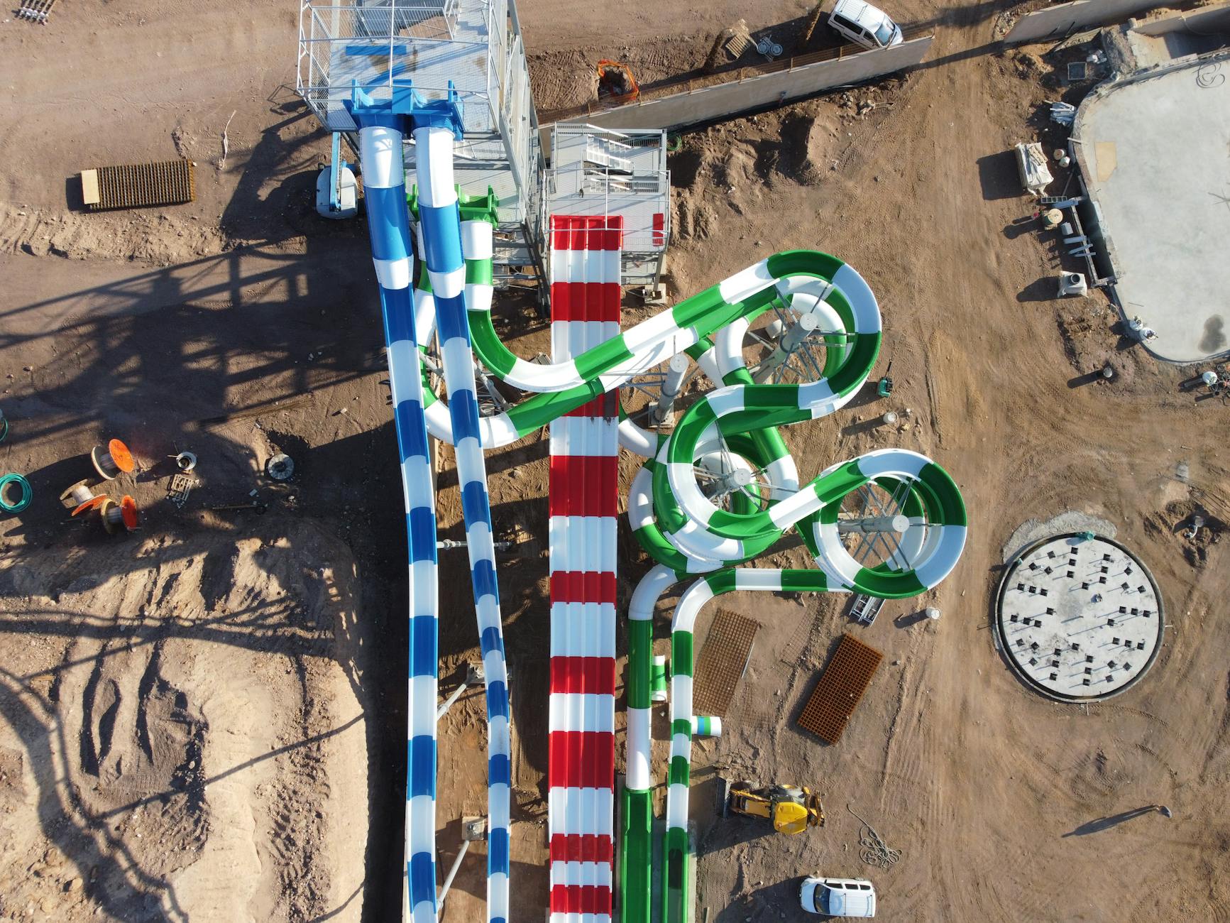 Drone shot of vibrant water slides under construction in a sunny outdoor water park.