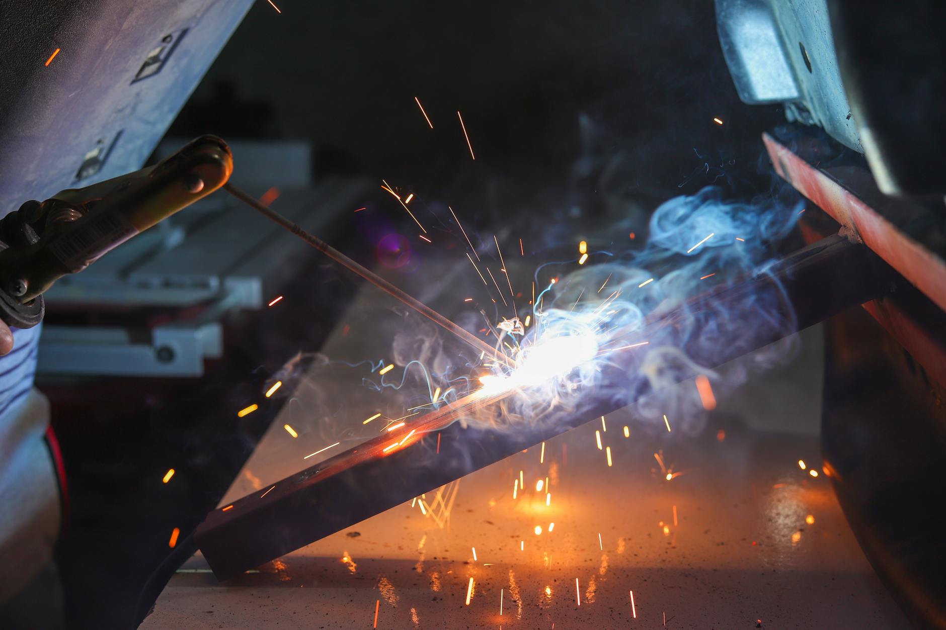 Close-up of a welder at work with sparks and smoke in an industrial setting.