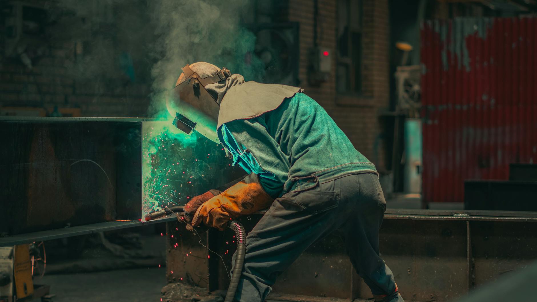 A welder in protective gear working in a factory, showcasing industrial skills and sparks.